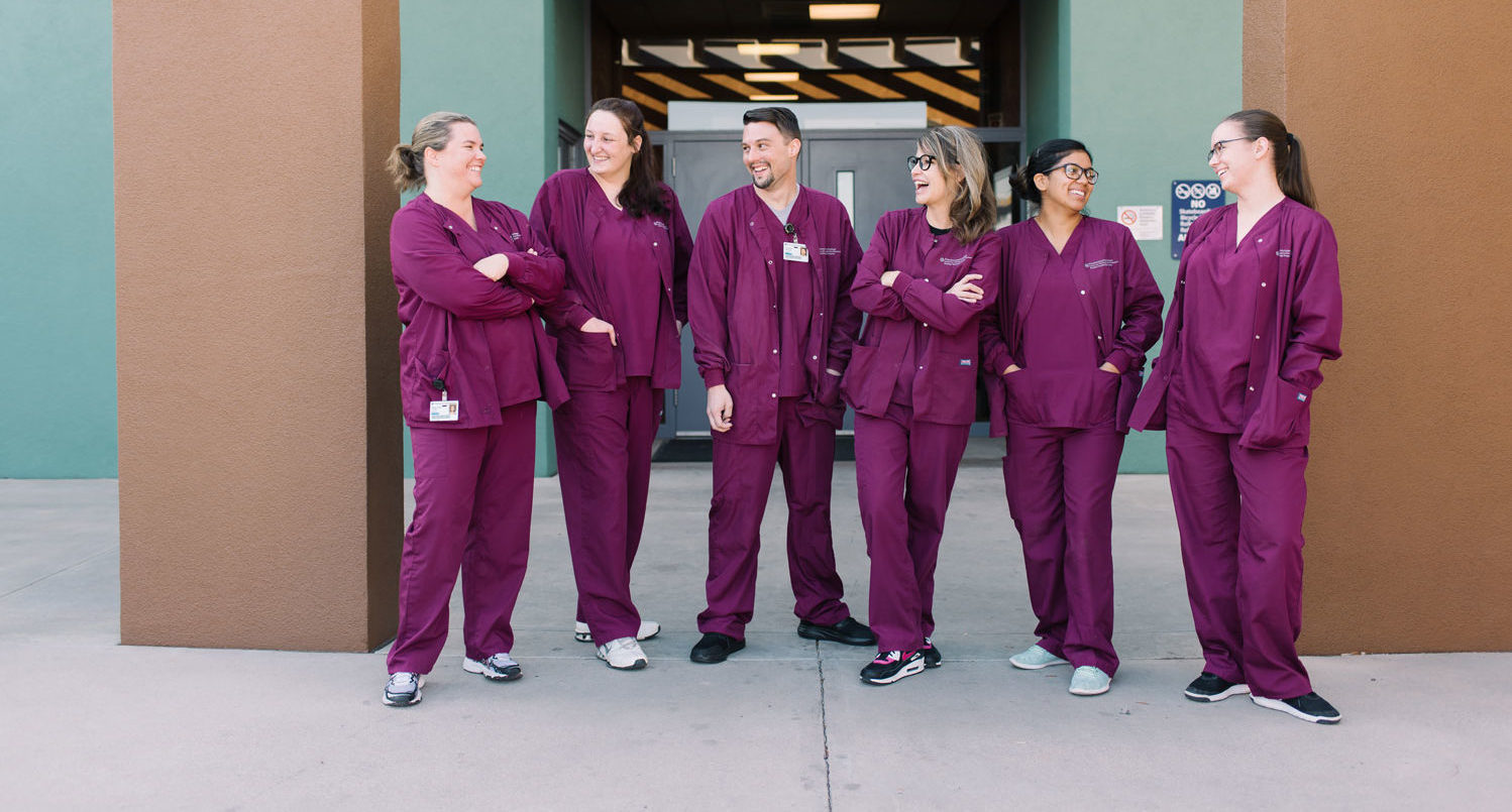 Students in purple scrubs smile outside a medical class