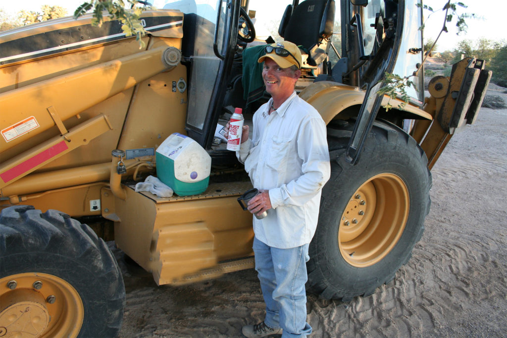 Man in baseball cap stands eating lunch beside a yellow tractor