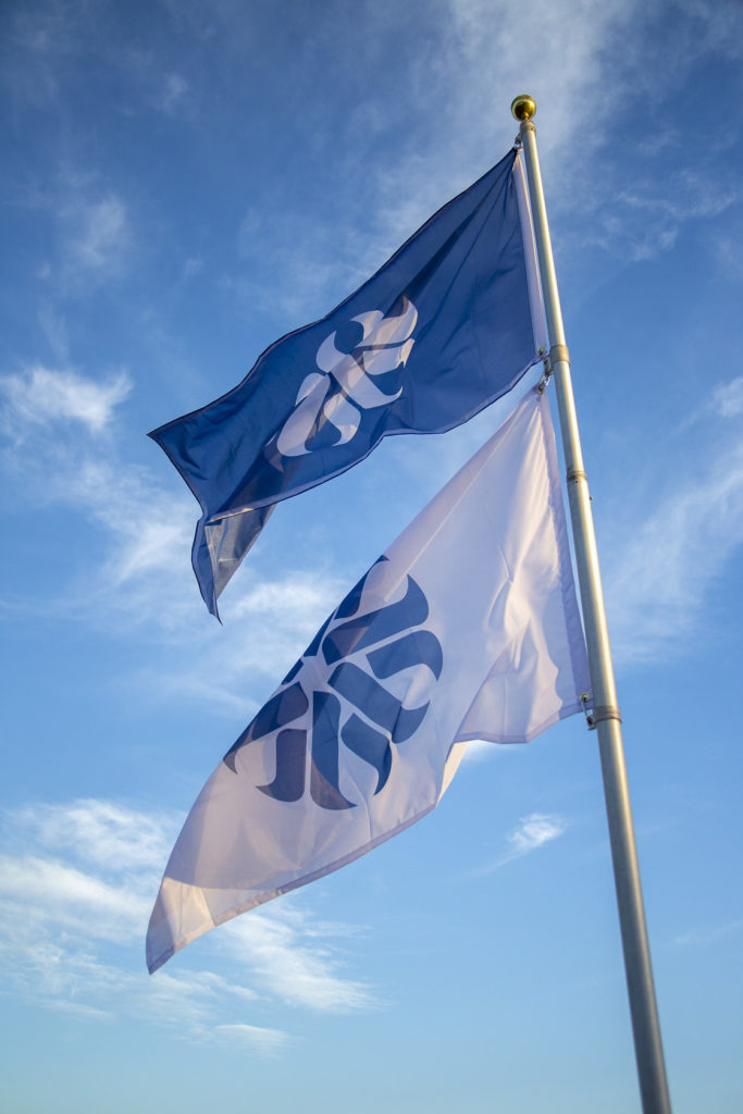 A blue and a white flag, both featuring the Pima Community College