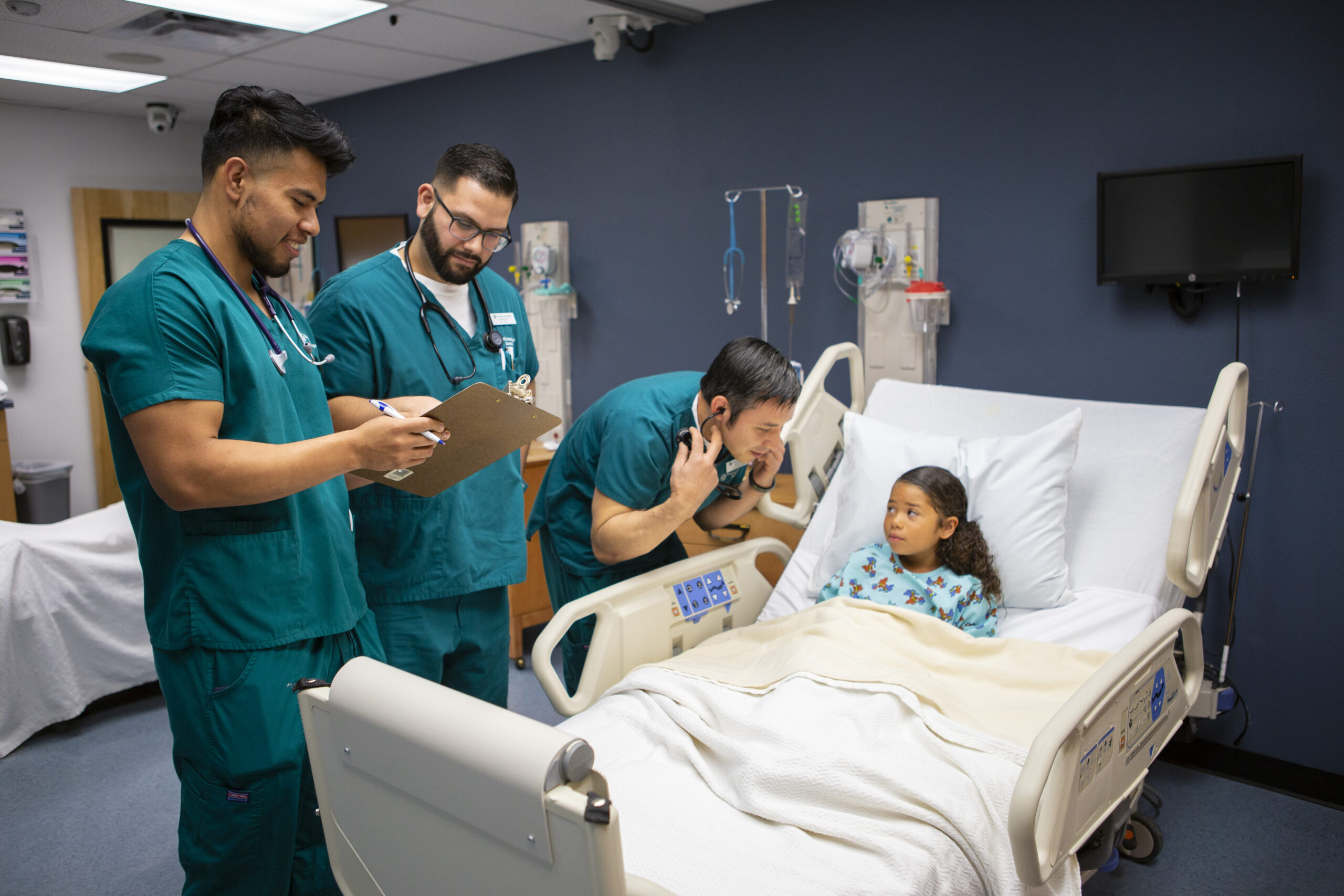 3 male nursing students assisting a young child in a hospital bed